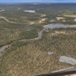 Aerial view of Crosswind Lake and the Prince William Sound Aquaculture Corporation field camp. The area is flat with a winding river in the middle in a forested, patchy area.