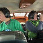Two people riding inside a small plane looking out the windows. One is using binoculars.