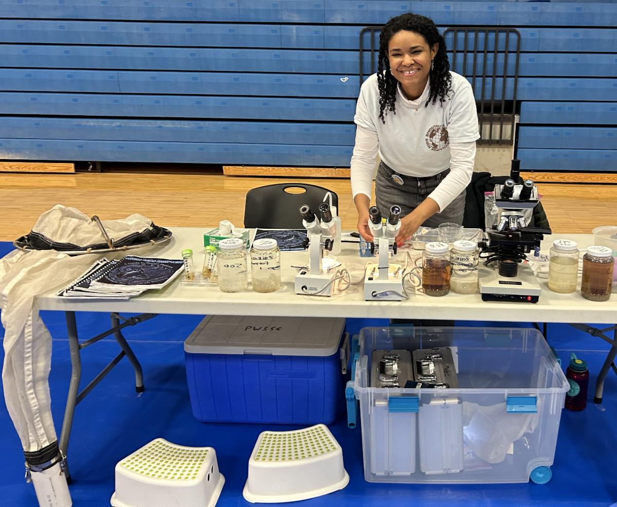 Woman standing at table full of scientific equipment: microscopes, nets, and more.