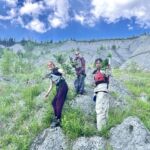 Stewards stopped for lunch and a weed picking break. They picked over 100 lbs of invasive white sweet clover. Three stewards standing on the bank of the river holding invasive weeds in their hands.