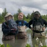 Three stewards pose in the Alaganik slough Three female stewards stand waste deep in the slough.