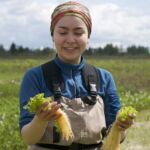 A steward looks at plants growing in the wetlands. A female steward holds plants in each hand while standing waste deep in the water. She is wearing waders.