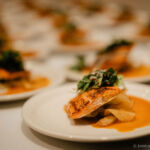 A grilled salmon filet on a bed of potato chips with an orange sauce on a circular white plate.