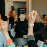 A group of guests at a banquet holding up plastic easter eggs.