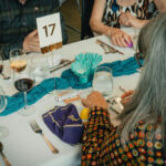 A close-up picture of a banquet table with blue flowers and decorations with a number stand and wine glasses half full.