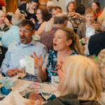 A crowd of people sitting at banquet tables and playing games at the Copper River Nouveau fundraiser at table 6.