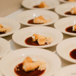 White bowls of cone shaped cream desserts with red sauce.