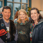 Three banquet attendees, one man on the left and two women on the right, standing in front of a window.